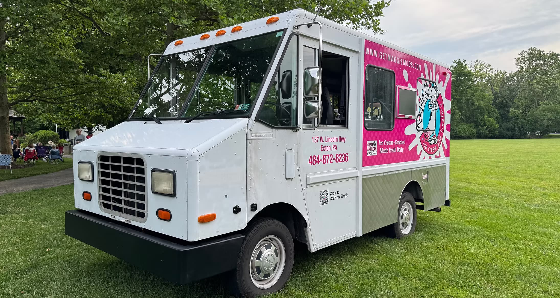The Maggie Moo's ice cream truck parked on the grass at an Exton event, magenta wrap and cow logo on the side